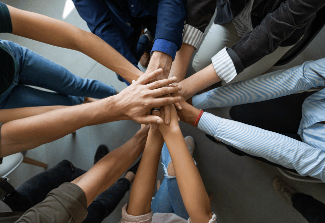 A group of people place their hands together in a circle, symbolizing unity and teamwork.