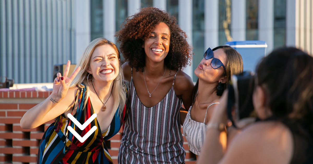 Three friends posing for a photo on a rooftop. One is making a peace sign, another is smiling broadly, and the third is puckering their lips while wearing sunglasses.